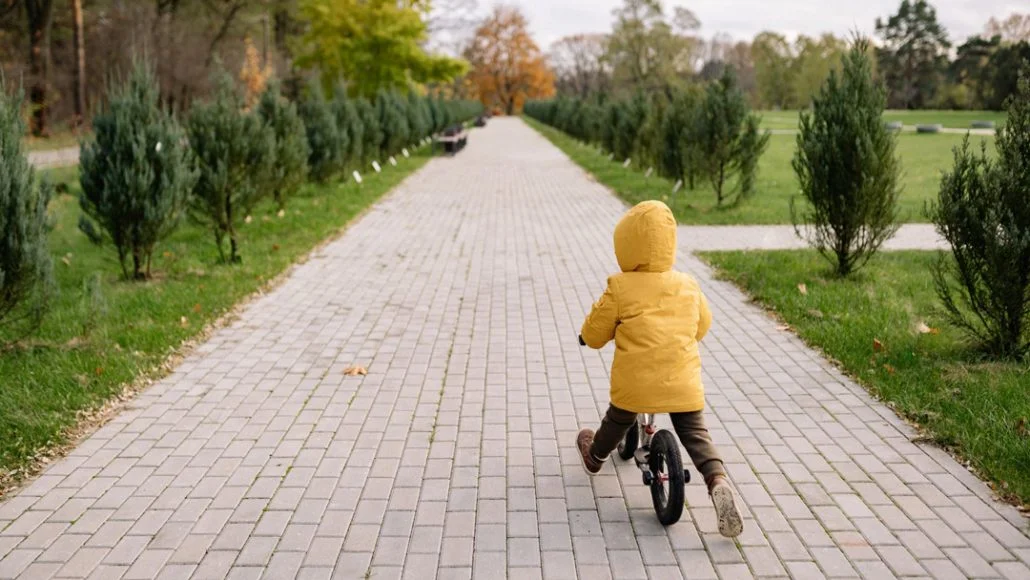 Fotografía de un niño sobre una bicicleta sin pedales en un parque de una ciudad